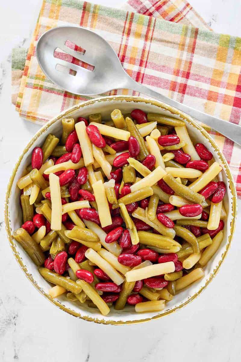 Grandma's three bean salad and a slotted spoon beside it.