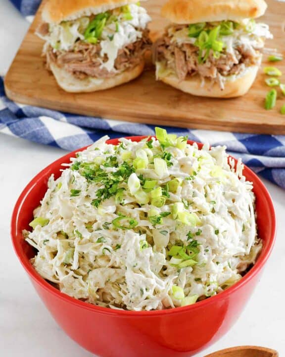 Copycat Houston's coleslaw in a bowl and two pork sliders with it on a wood board.