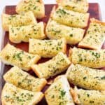 Homemade Brennan's garlic bread slices scattered on a wood board.