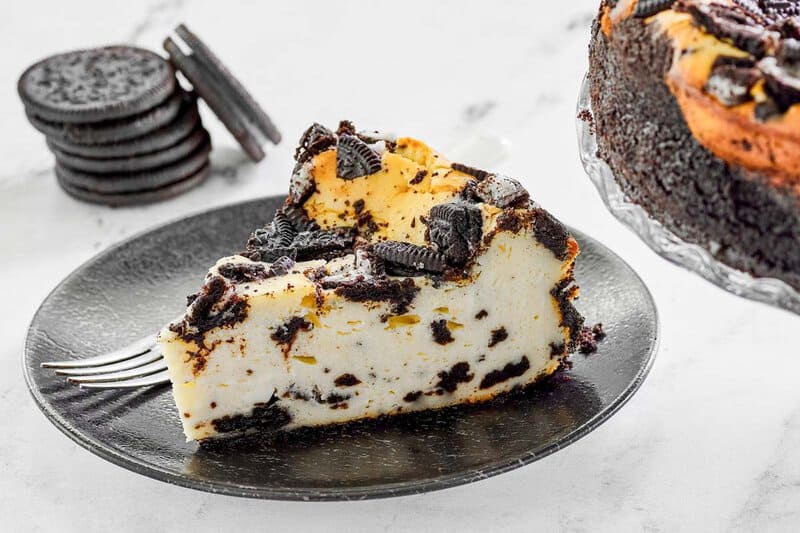 A slice of Cheesecake Factory Oreo cheesecake and oreos stacked behind it.