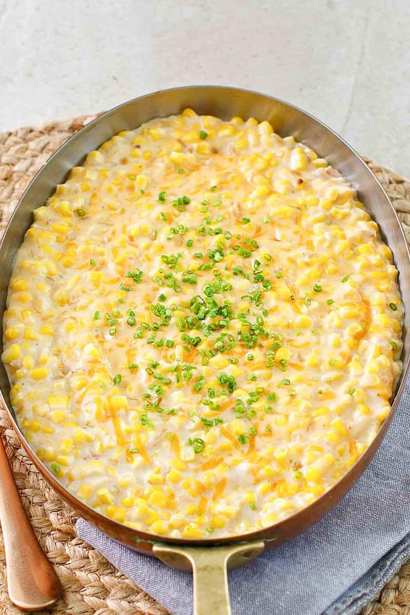 Cheesy creamed corn in a skillet and a kitchen towel.