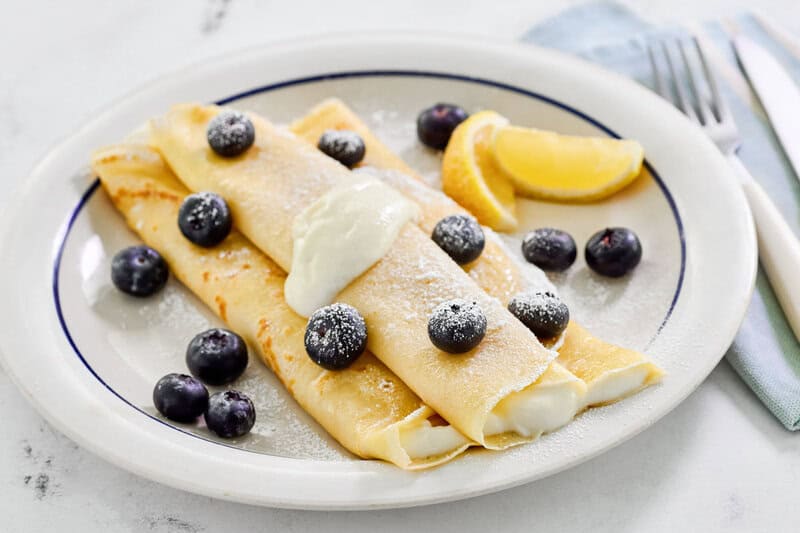 Copycat ihop lemon ricotta crepes, lemon wedges, and blueberries on a plate.