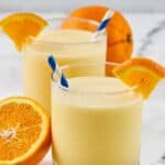 Homemade orange julius in two glasses and fresh oranges.