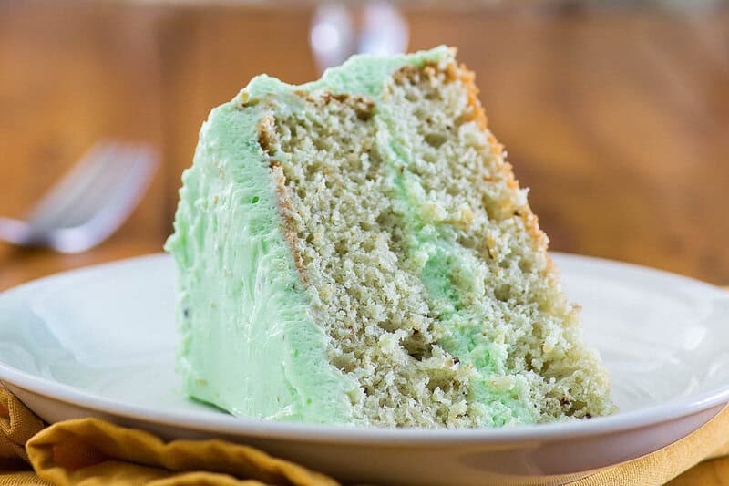 A slice of pistachio cake on a plate and a fork behind it.