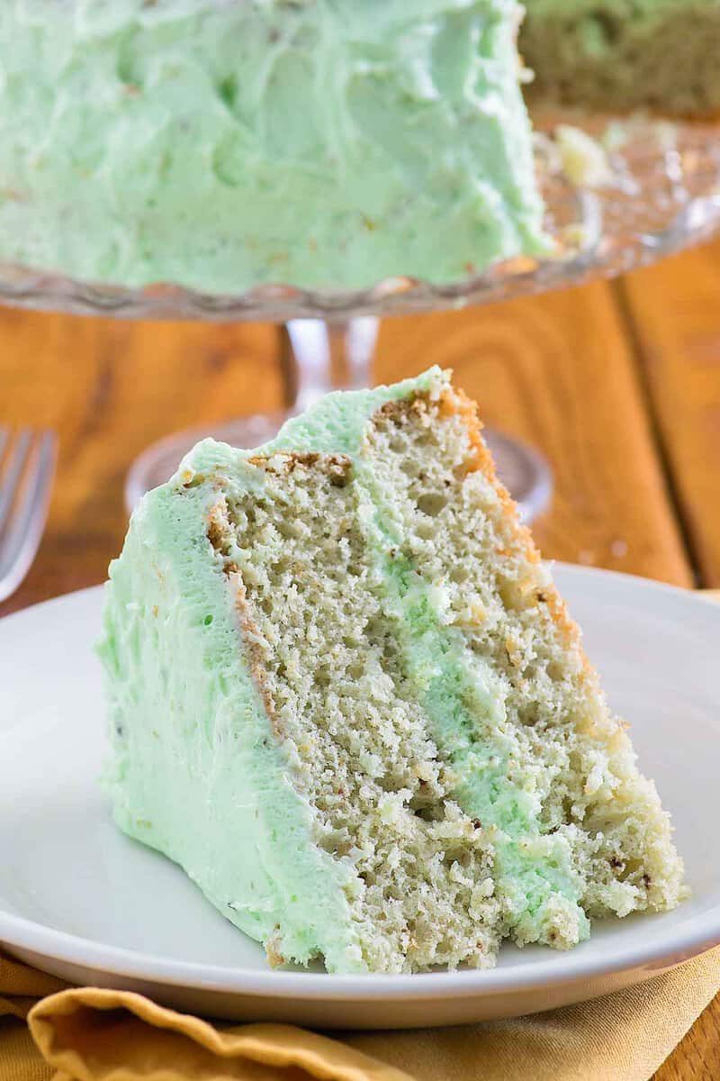 A slice of homemade pistachio cake and the cake on a cake stand.