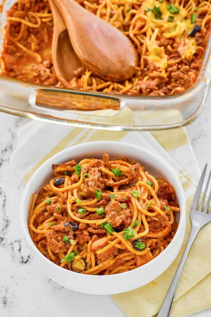 Taco spaghetti casserole in a baking dish and a serving in a bowl.