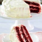 Homemade waldorf astoria red velvet cake on a cake stand and a slice on a small plate.