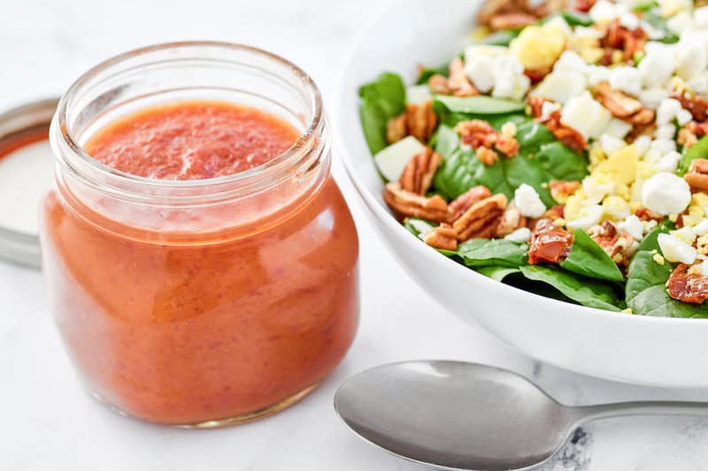 Copycat Bennigan's hot bacon dressing in a jar next to a salad.