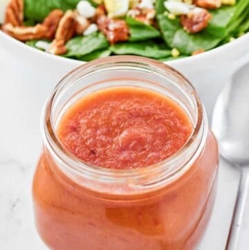 Copycat Bennigan's hot bacon dressing in a jar and a salad behind it.