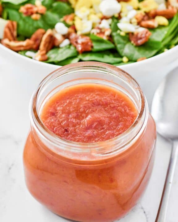 Copycat Bennigan's hot bacon dressing in a jar and a salad behind it.