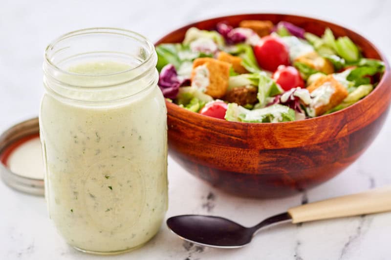 A jar of homemade buttermilk ranch dressing next to a salad.