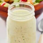 Homemade buttermilk ranch dressing in a glass mason jar and a salad behind it.