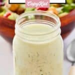 Homemade buttermilk ranch dressing in a jar in front of a salad.