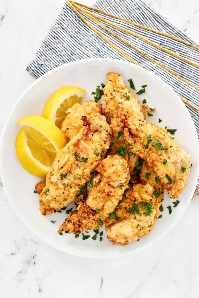 Copycat Piada fried chicken tenders and lemon wedges on a plate.