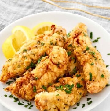 Copycat Piada chicken tenders and lemon wedges on a plate.