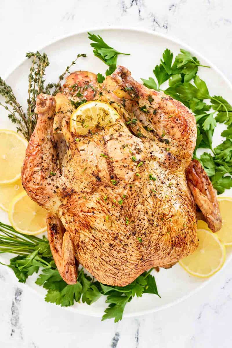 Oven roasted whole chicken, fresh herbs, and lemon slices on a round platter.