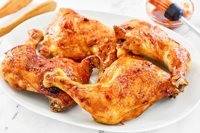 Honey sriracha glazed chicken leg quarters on a platter and the glaze in a small glass bowl.