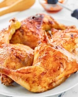 Sriracha honey glazed chicken leg quarters on a platter and glaze in a small bowl.