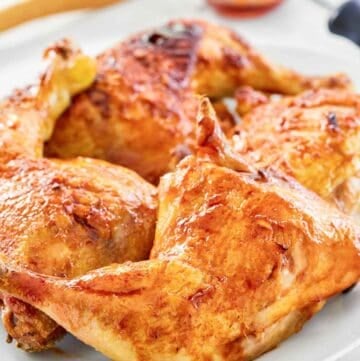 Sriracha honey glazed chicken leg quarters on a platter and glaze in a small bowl.