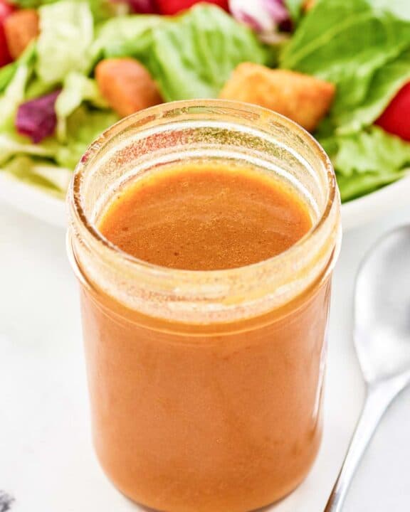 Copycat state fare lemon vinaigrette salad dressing in a jar and a salad behind it.