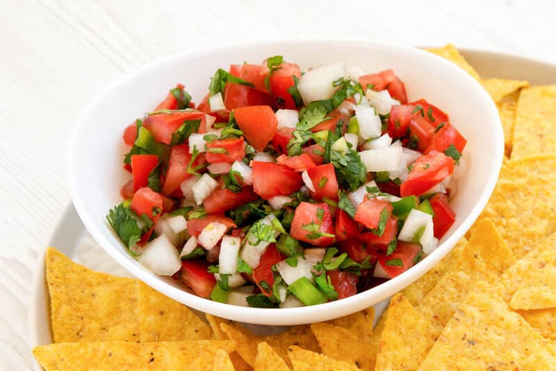 A bowl of copycat TGI Friday's pico de gallo and tortilla chips on a plate.