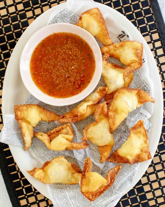 Cream cheese wontons and dipping sauce on a parchment paper covered platter.