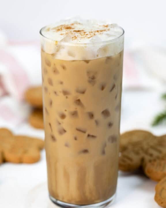 Copycat Starbucks gingerbread oat milk chai latte in a tall glass and cookies behind it.