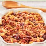 Crockpot calico beans in a serving dish and a wooden spoon behind it.