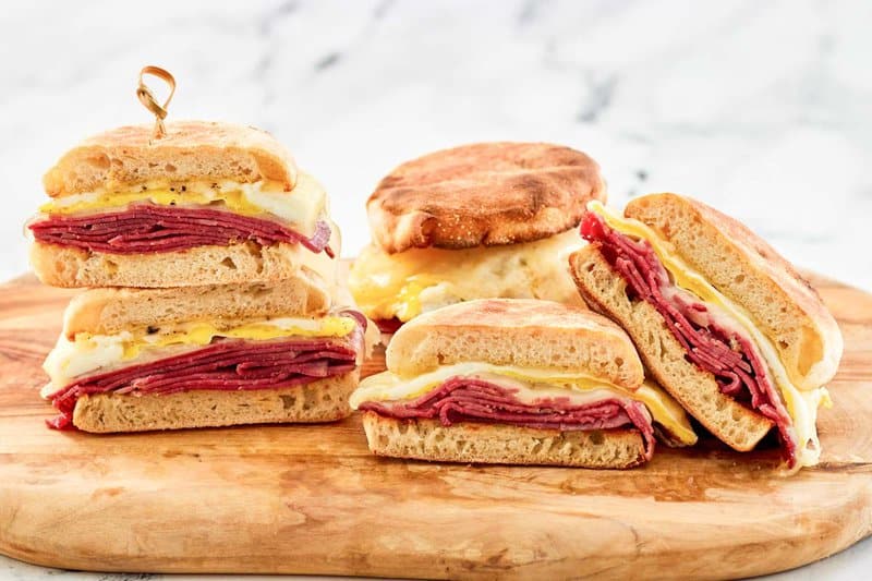 Three corned beef breakfast sandwiches on a wood serving board.