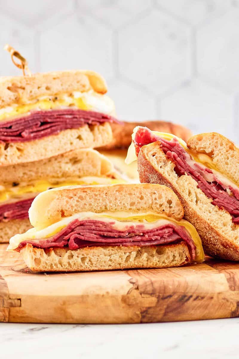 Homemade corned beef breakfast sandwiches cut in half and on a wood board.