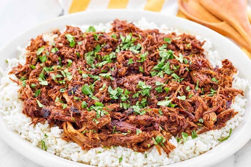 Instant pot pulled pork on a platter and wooden serving spoons behind it.