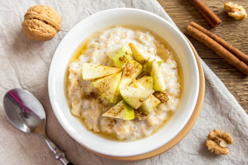 Apple cinnamon oatmeal in a bowl, cinnamon sticks, and walnuts.