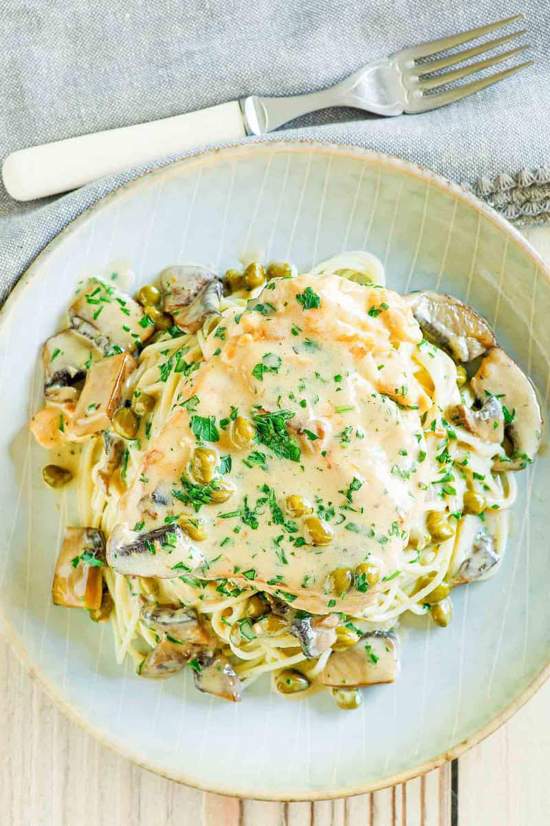 Copycat Cheesecake Factory chicken piccata over pasta on a plate and a fork.