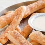 Homemade Domino's cinnastix and a small cup of icing dipping sauce next to them.