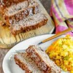 Copycat Cracker Barrel meatloaf slices on a plate in front of the meatloaf.