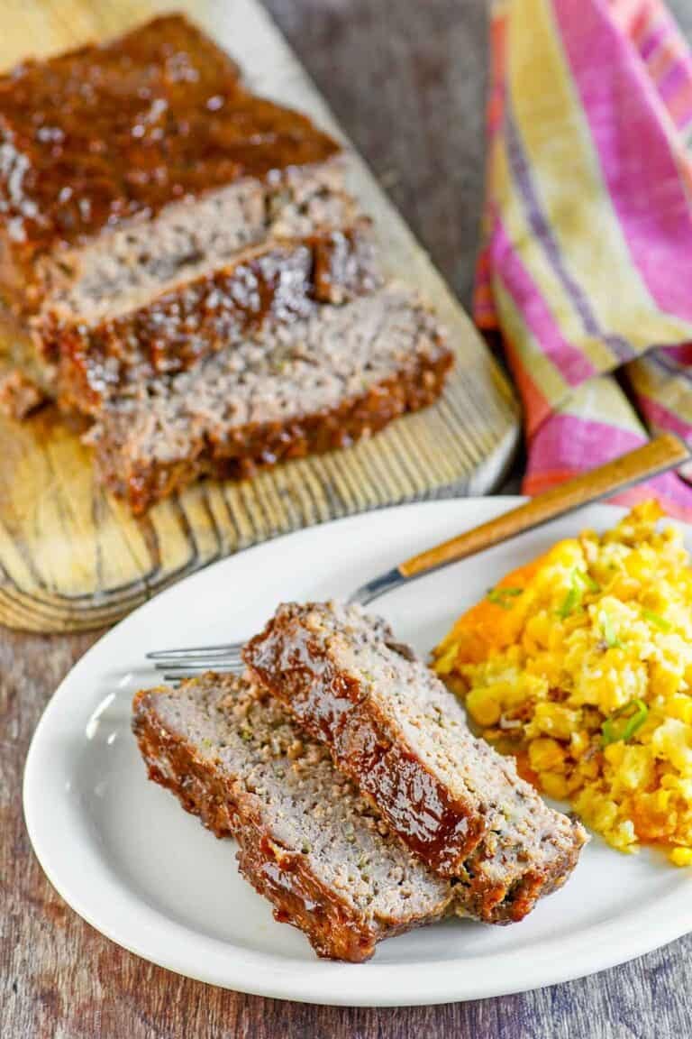 Copycat Cracker Barrel meatloaf slices on a plate in front of the meatloaf.