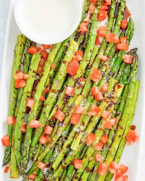Copycat olive garden parmesan roasted asparagus with dipping sauce on a platter.