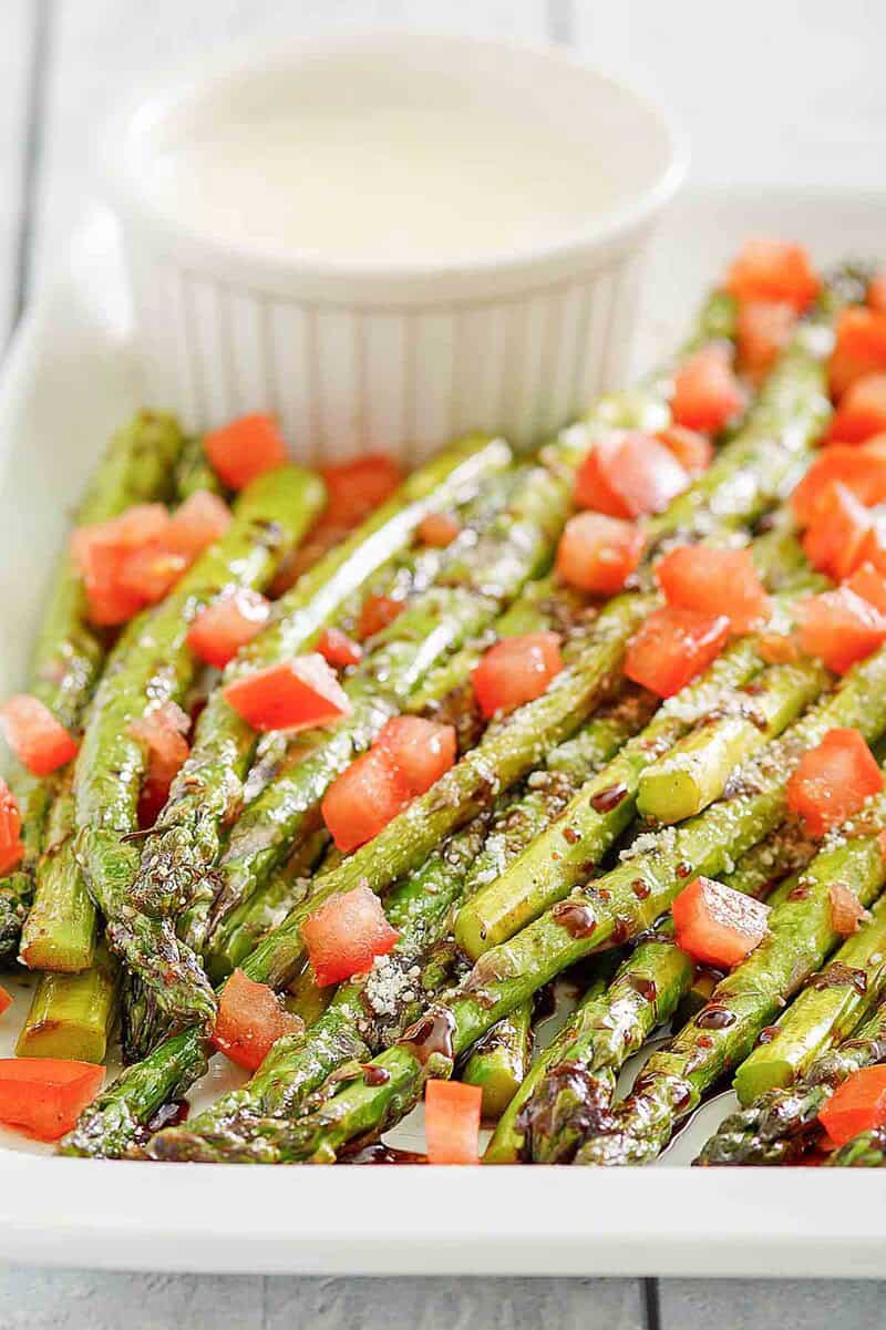 Copycat olive garden parmesan roasted asparagus with a small cup of dipping sauce.