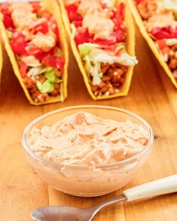 Copycat Taco Bell chipotle sauce in a small bowl, a spoon, and tacos.