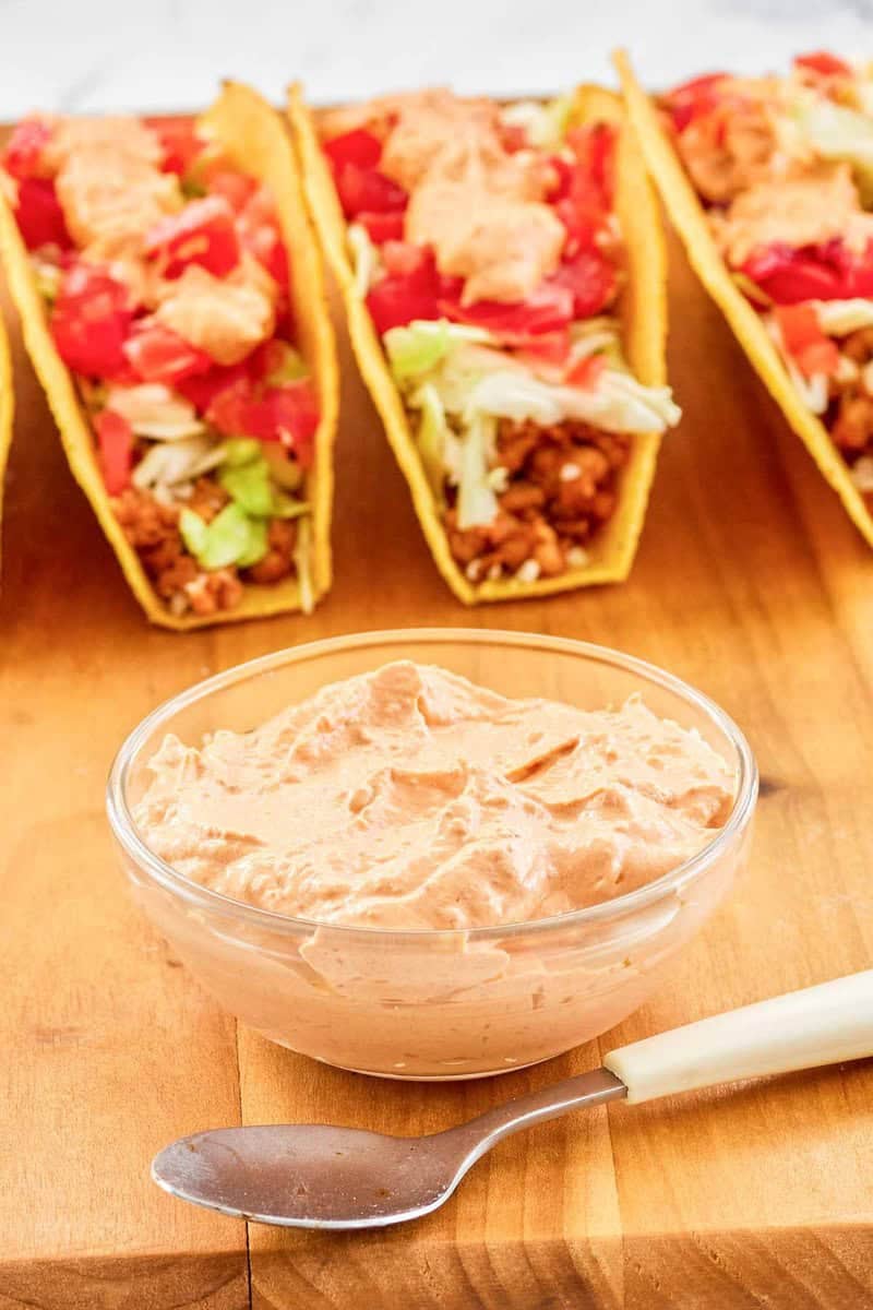 Copycat Taco Bell chipotle sauce in a small bowl, a spoon, and tacos.