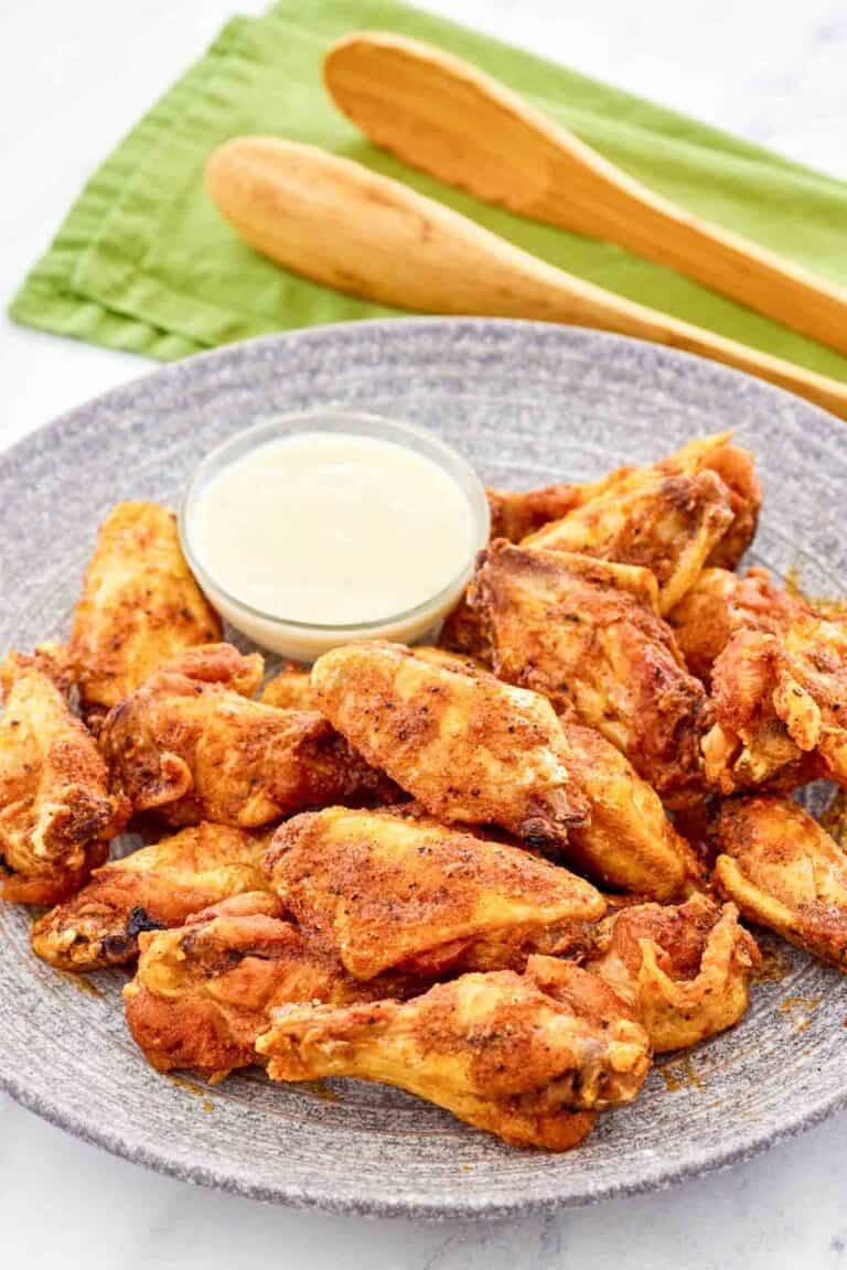 Copycat Wingstop Louisiana rub wings and a small cup of dipping sauce on a plate.