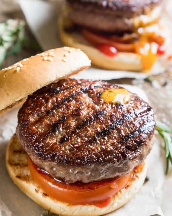 Grilled backyard burger with tomato on a sesame seed bun.