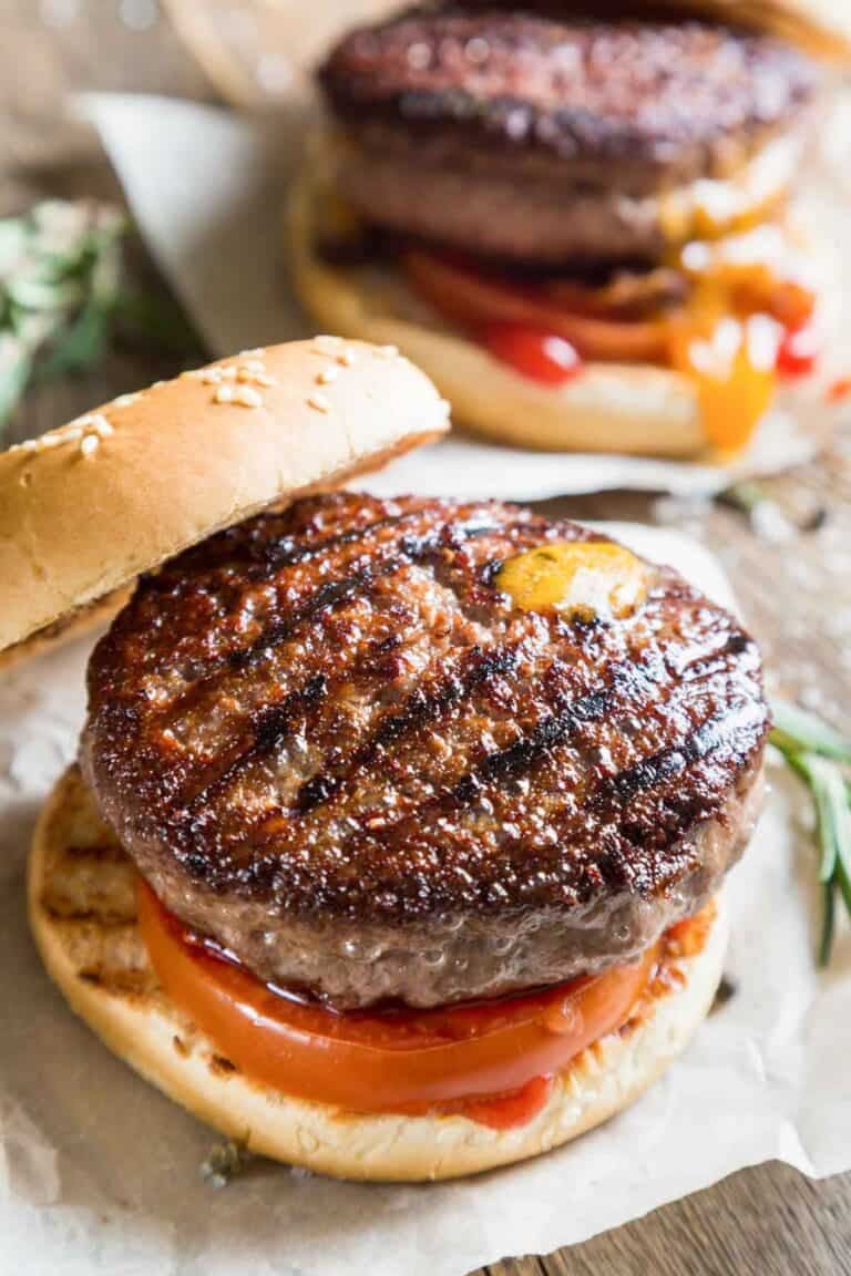 Grilled backyard burger with tomato on a sesame seed bun.
