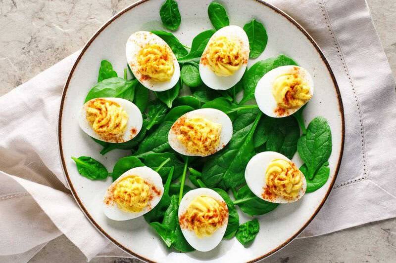 Classic deviled eggs over spinach leaves on a plate and a cloth napkin underneath it.