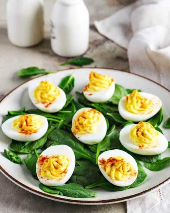 Classic deviled eggs over spinach leaves on a plate.