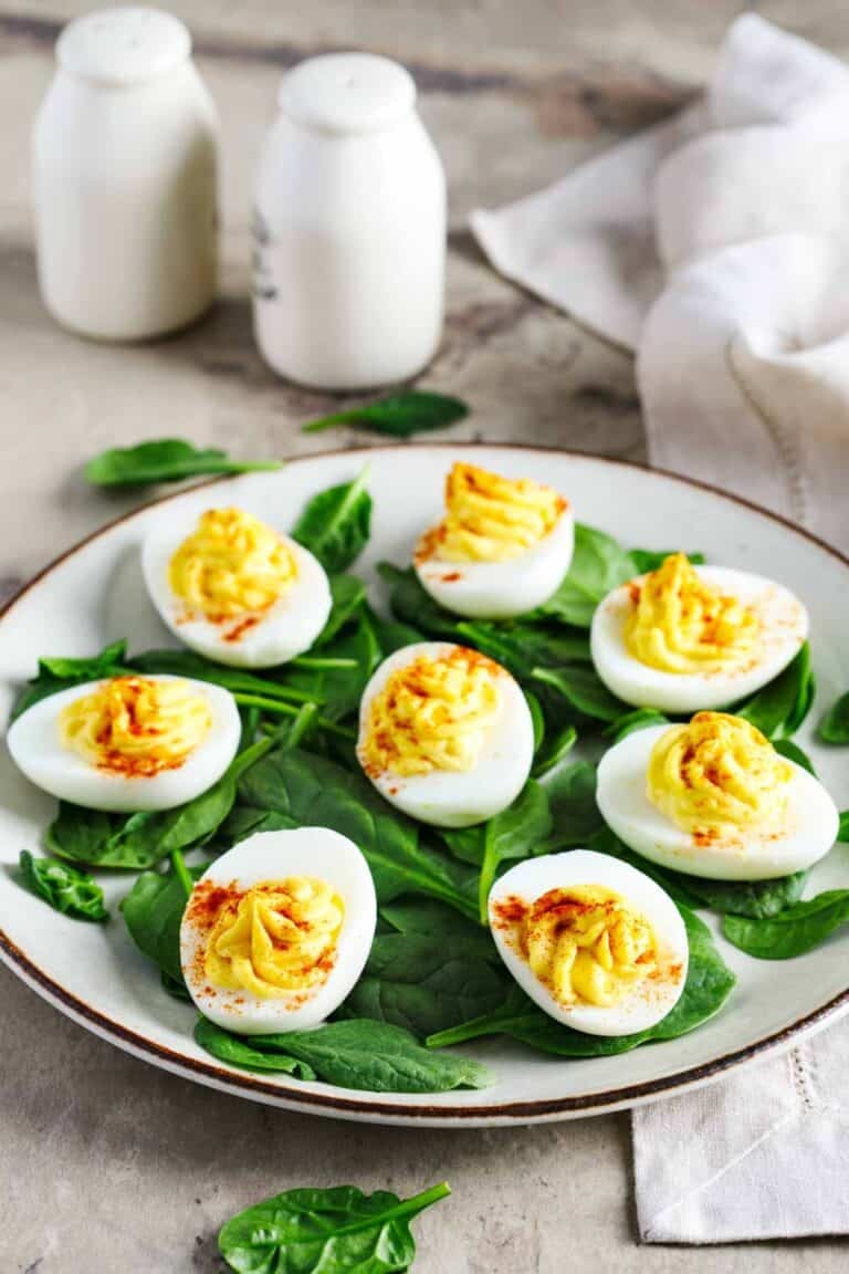 Classic deviled eggs over spinach leaves on a plate.