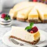 New York style cheesecake slice on a plate and the cheesecake behind it.