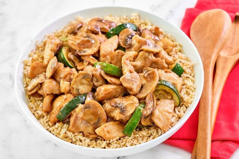 Copycat Panda Express mushroom chicken over rice and wood serving utensils.