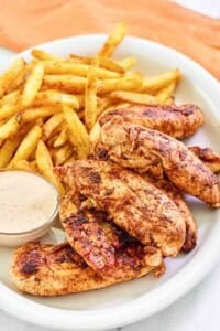 Copycat Popeyes blackened chicken tenders served with fries and dipping sauce.