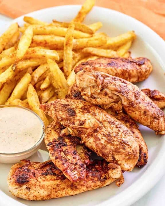 Copycat Popeyes blackened chicken tenders served with fries and dipping sauce.